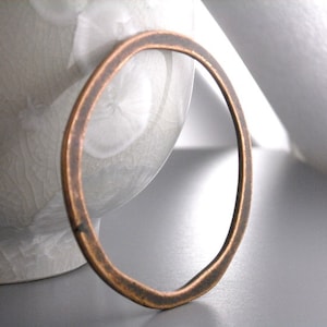 May include: A simple, rustic copper bangle bracelet. The bracelet is made of a single piece of copper that has been hammered and shaped into a circle. It has a slightly irregular shape and a warm, aged patina.