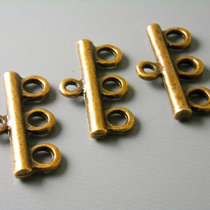 May include: Three antique gold-toned metal connector clasps for jewelry making. Each clasp has a long bar with three round loops.