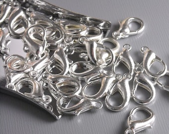 May include: A close-up of a pile of silver-toned metal lobster claw clasps. The clasps are scattered on a gray surface.