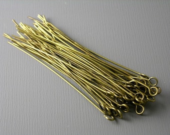 May include: A collection of numerous brass-toned metal eye pins, each featuring a straight, slender shaft and a small, circular loop at one end, arranged in a loose, overlapping cluster.