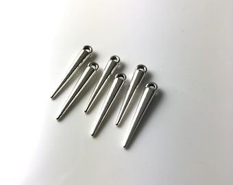 Op de afbeelding: Zes zilverkleurige metalen kegelvormige bedels met een lus aan de bovenkant. De bedels zijn in een rij gerangschikt, met de punten van de kegels in dezelfde richting.