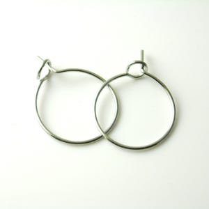 May include: A pair of silver-colored hoop earrings. Each earring is a simple, circular design with a small loop at the top for attachment. The earrings are displayed against a plain white background, highlighting their minimalist style.