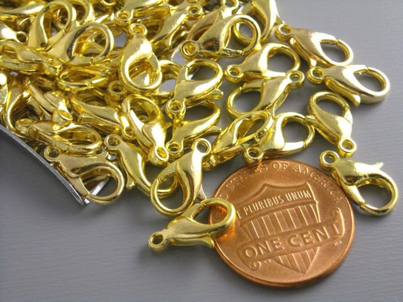 May include: A pile of gold-toned metal lobster claw clasps, some are open and some are closed. A US penny is included for size reference.