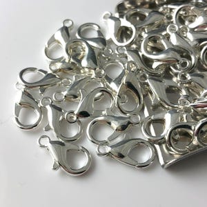 May include: A pile of silver-toned lobster claw clasps, commonly used for jewelry making.