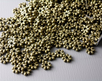 May include: A large pile of antique gold metal spacer beads with a flower-shaped design. Each bead has a small hole in the center.