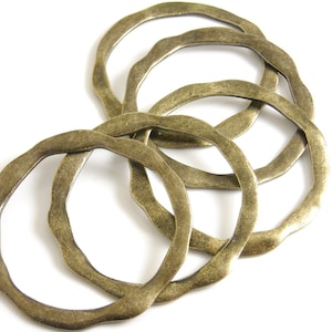 May include: Five brass rings with a wavy, irregular edge. The rings are stacked on top of each other, with the largest ring at the bottom and the smallest ring at the top.