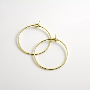 May include: Two gold-colored hoop earrings. The earrings are circular, with a simple, elegant design. The hoops are thin and appear to be made of metal. The earrings are displayed on a white background.