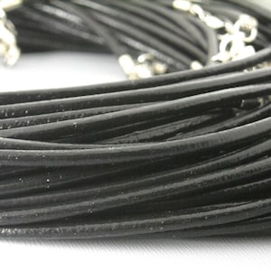 May include: A close-up of a bundle of black leather cord, showing the texture and smooth finish. The cord is arranged in a circular pattern, with the ends of the cord visible.