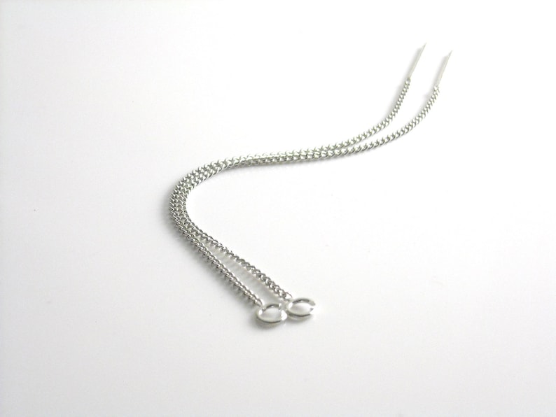 May include: A pair of silver chain earrings with a simple design. The earrings are long and dangle from the earlobe.