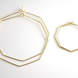 May include: Two pairs of gold-colored geometric hoop earrings. One pair is larger, with a double-layered design, and the other is smaller, with a single layer. Both have a modern, minimalist style.