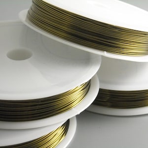 May include: Close-up of several spools of gold-colored wire. The wire is tightly wound on white plastic spools. The spools are stacked, with some partially visible. The wire appears to be for jewelry making or crafts.