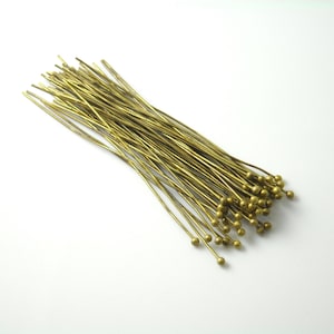 May include: A bundle of gold-toned head pins with round heads. The pins are approximately 1 inch long.