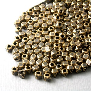 May include: A pile of antique gold metal beads with a faceted diamond shape. Each bead has a hole in the center for stringing.