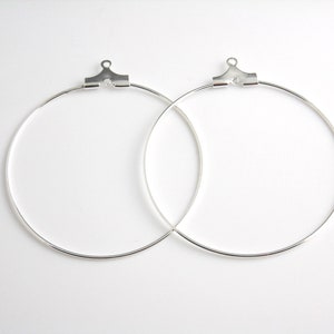May include: Two silver hoop earrings with a hinged closure. The hoops are approximately 2 inches in diameter.