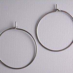 May include: Two silver hoop earrings with a simple, circular design. The earrings are made of thin metal and have a smooth finish.