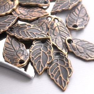 May include: A pile of antique gold leaf charms with a detailed leaf design. The charms have a hole at the top for attaching to jewelry or other crafts.
