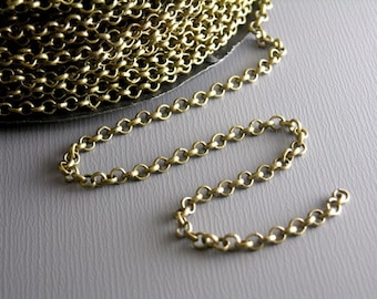 May include: Close-up of a roll of antique brass-colored chain. The chain is made of small, round links. A length of the chain is unrolled, lying on a gray surface. This chain is suitable for jewelry making and craft projects.