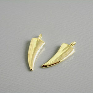 May include: Two gold-colored metal charms shaped like a pointed horn. The charms have a smooth, shiny finish.