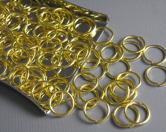 May include: A large quantity of gold-colored metal jump rings. The rings are scattered on a silver surface and some are spilling over the edge.