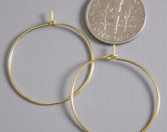 May include: Two gold hoop earrings with a simple, circular design. The earrings are shown next to a US dime for size comparison.