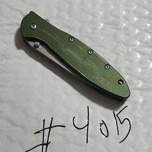 May include: A green folding pocket knife with a silver blade. The knife has a textured handle and is labeled "Kershaw". The number "4015" is handwritten below the knife.