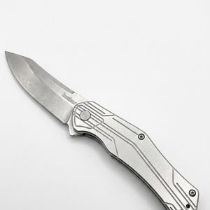May include: A silver folding knife with a textured blade and handle. The blade has a unique pattern, and the handle features a linear design. The brand name "Kershaw" is visible on the blade.