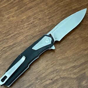 May include: A silver and black folding knife with a partially serrated blade. The knife has a black handle with a silver pocket clip and the brand name "Kershaw" printed on it. The blade is approximately 3 inches long.