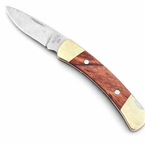 May include: A folding pocket knife with a stainless steel blade and a wooden handle. The handle is accented with brass bolsters and rivets. The blade is marked "BUCK USA".