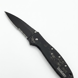 May include: Black folding knife with a serrated edge and a pointed tip. The handle has a textured appearance with visible rivets. The text "DWK Kershaw" is printed on the handle.
