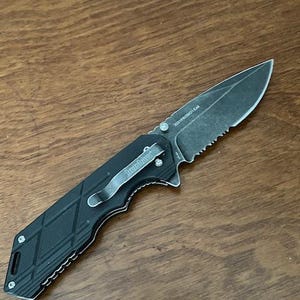 May include: Black folding knife with a partially serrated blade. The knife has a textured black handle with a silver pocket clip that reads "Kershaw". The blade has the text "2021PROMO GEAR".