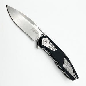 May include: A silver and black folding knife with a partially serrated blade. The knife features the brand name "Kershaw" on the blade. The handle is black with silver accents.