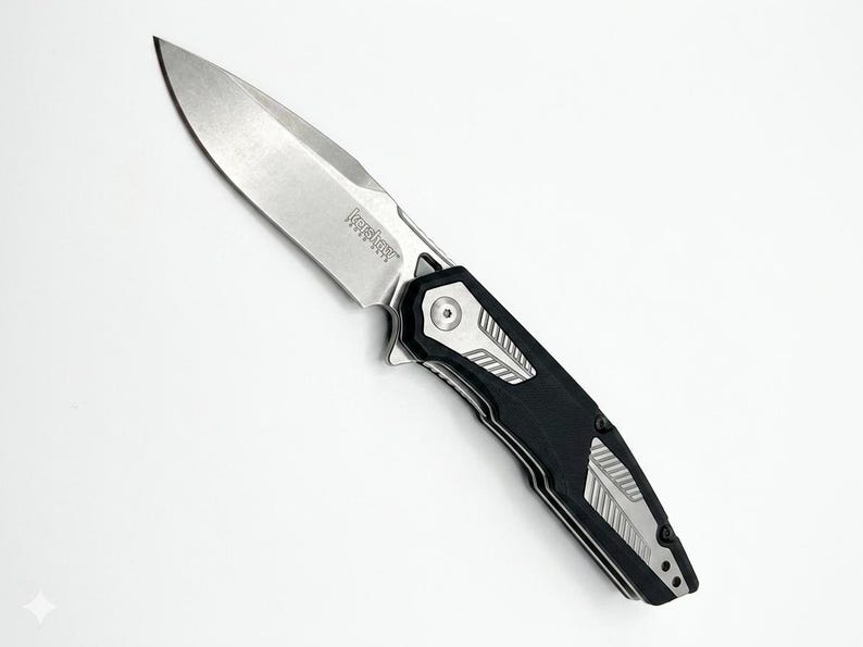 May include: A silver and black folding knife with a partially serrated blade. The knife features the brand name "Kershaw" on the blade. The handle is black with silver accents.