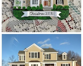 Puede incluir: Un adorno navideño que representa una casa de dos pisos con un exterior de color beige, molduras blancas y contraventanas negras. El adorno tiene una pancarta que dice "Navidad 2018".