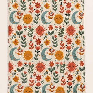 May include: A rectangular blanket featuring a repeating pattern of smiling suns in orange and red, crescent moons in muted blue, and various stylized flowers in shades of red, orange, and green against a cream-colored background.