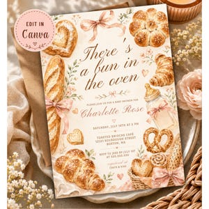 Peut inclure: Invitation de baby shower avec des illustrations à l'aquarelle de pains et de viennoiseries. Le texte dit "There's a bun in the oven" et invite les invités à célébrer Charlotte Rose. Date, heure et lieu inclus.