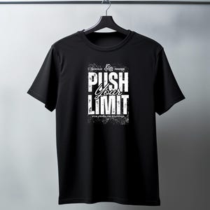 Puede incluir: Camiseta negra de cuello redondo con el texto "PUSH YOUR LIMIT" en blanco, con un efecto desgastado. La camiseta tambi&eacute;n presenta texto adicional en la parte superior e inferior. La camiseta est&aacute; colgada de una percha negra.