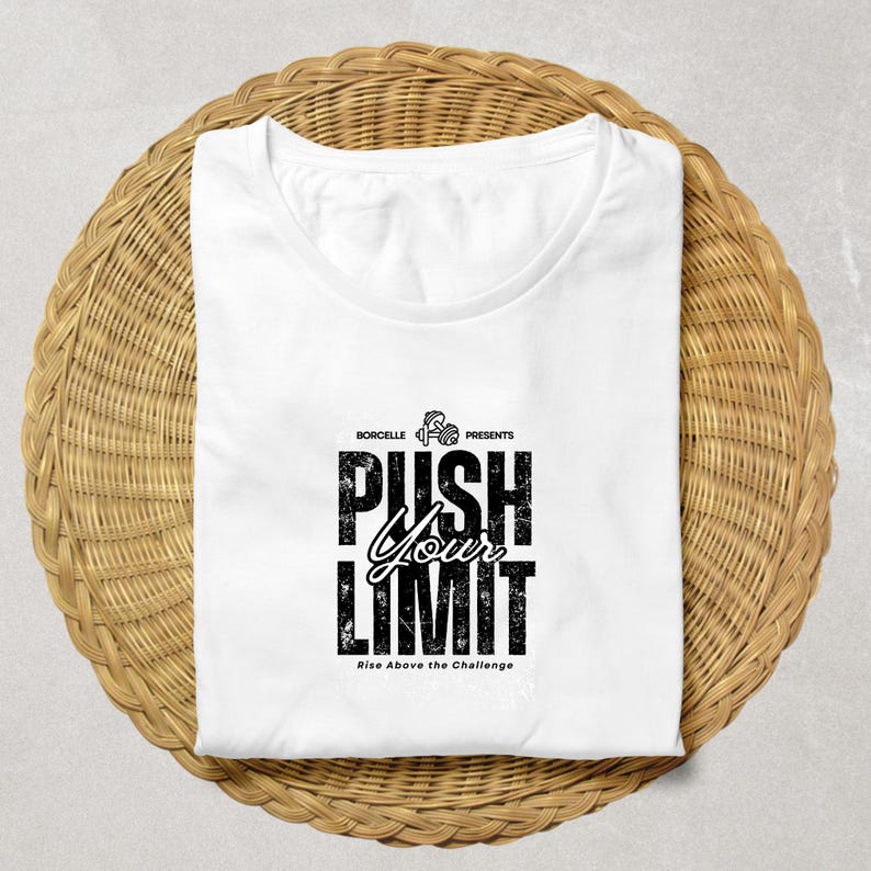 Puede incluir: Camiseta blanca con el texto "PUSH YOUR LIMIT" en una fuente negra desgastada. La camiseta tambi&eacute;n incluye el texto "Rise Above the Challenge" y la marca "BORCELLE PRESENTS". La camiseta est&aacute; doblada sobre una superficie circular tejida.