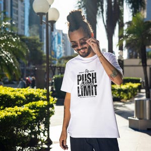 Puede incluir: Camiseta blanca con el texto "PUSH YOUR LIMIT" en fuente negra estilizada. La camiseta tiene cuello redondo y mangas cortas. La imagen est&aacute; tomada al aire libre con una persona que lleva gafas de sol.
