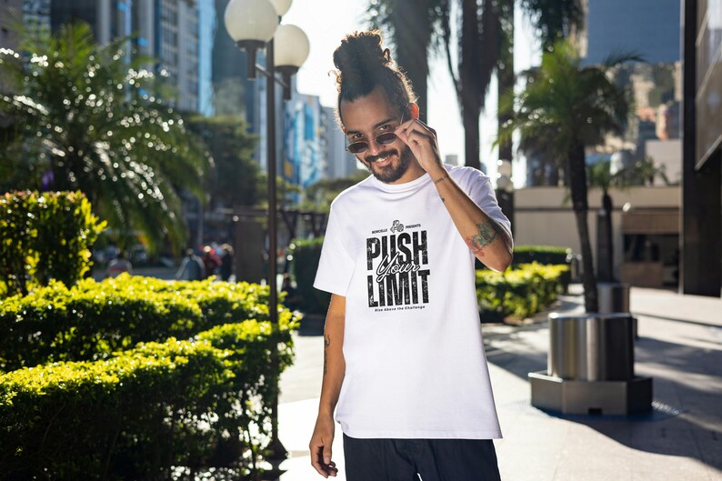 Puede incluir: Camiseta blanca con el texto "PUSH YOUR LIMIT" en fuente negra estilizada. La camiseta tiene cuello redondo y mangas cortas. La imagen est&aacute; tomada al aire libre con una persona que lleva gafas de sol.