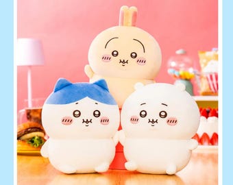 May include: Three plush toys: a yellow bunny, a white bear, and a white cat with blue ears. Each has a round body, small arms, and a cute face with rosy cheeks. The bunny is in the back, the bear and cat are in the front.