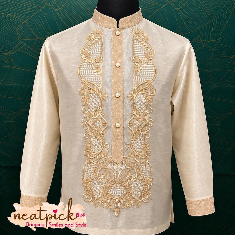 May include: A cream-colored long-sleeve barong shirt featuring a mandarin collar, a button-down placket, and intricate gold embroidery along the front panels. The fabric has a subtle sheen, and the text neatpick shop Bringing Smiles and Style is visible.