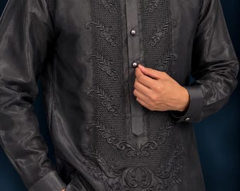 May include: A charcoal gray long-sleeved shirt featuring a mandarin collar, a button-down front placket, and intricate tonal embroidery along the chest panel. The garment is crafted from a semi-sheer fabric with a subtle sheen.