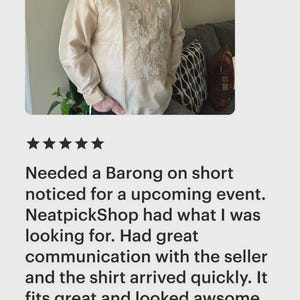 May include: A cream-colored long-sleeved barong shirt featuring a mandarin collar, a button-down front placket, and intricate white floral embroidery detailing along the center panel and cuffs, constructed from a semi-sheer fabric.