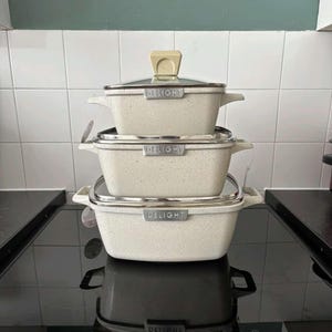 May include: Three stacked off-white speckled cooking pots with lids and handles. Each pot has a silver rim and the word "DELIGHT" printed on the front. The pots are on a black hob.