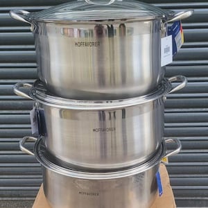 Puede incluir: Una pila de tres ollas de cocina de acero inoxidable con tapas y asas. Las ollas están etiquetadas como "HOFFAVORER" y están sobre una caja de cartón. El fondo es una superficie oscura con líneas horizontales.