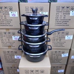 Könnte beinhalten: Ein Stapel schwarzer Kochgeschirrsets mit Glasdeckeln und Griffen, mit der Aufschrift "IBRAA". Die Sets werden auf Kartons präsentiert, die jeweils mit Produktinformationen versehen sind, einschließlich Maßen von 36x36x32,5 cm.