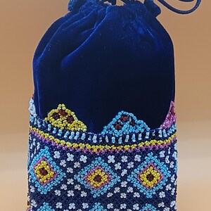 May include: A dark blue velvet drawstring bag with a beaded design. The bag features a geometric pattern in shades of blue, yellow, and pink. The top of the bag is a solid dark blue velvet, and the drawstring is a matching dark blue cord.