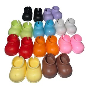 May include: A collection of colorful plastic doll shoes in various shades, including black, purple, green, blue, white, red, orange, pink, yellow, and brown. The shoes are arranged in rows and columns.