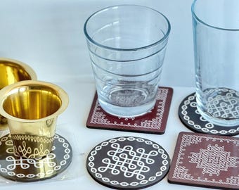 May include: A collection of drinkware and coasters. Two clear drinking glasses sit on decorative coasters with white geometric patterns. Two brass containers and two additional coasters are also present. The coasters are brown and black.