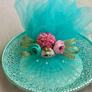 May include: A turquoise serving tray with a detailed lace design. The tray is decorated with pink, teal, and white flowers, gold ribbon, and a turquoise tulle bow. Small white pearls add a touch of elegance to the presentation.